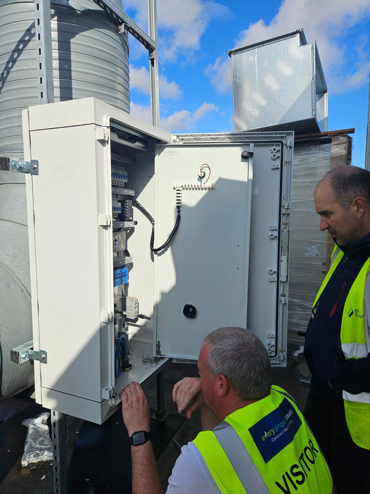 The outdoor BMS panel installed on the roof next to the plant, door open, with an SSE Energy Solutions engineer and a G&G visitor looking inside